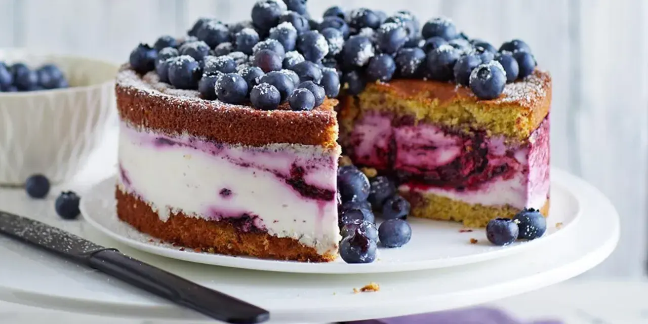 Saftige Heidelbeertorte mit Joghurt-Füllung, garniert mit frischen Beeren und Puderzucker. Ein Genuss für Augen und Gaumen.