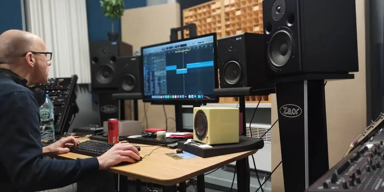 Producent muzyczny pracuje nad miksem i masteringiem w domowym studio. Na ekranie widać sekwencer, a wokół monitory studyjne.