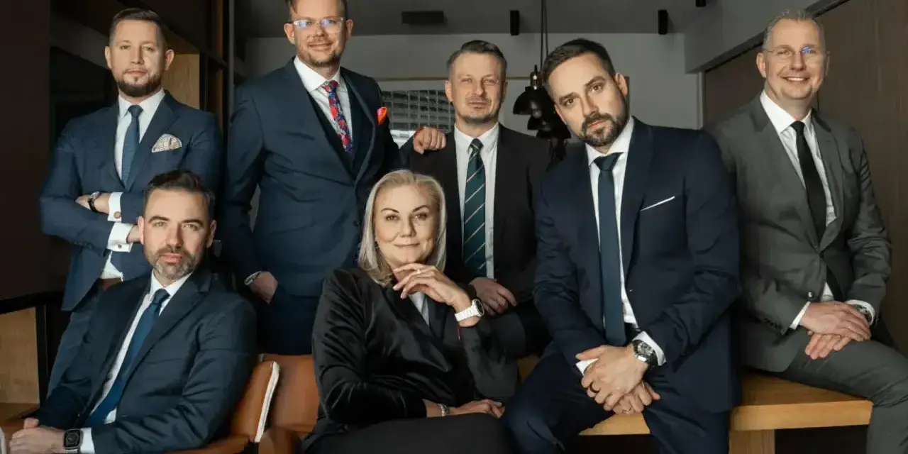 Grupa profesjonalistów w garniturach, w tym jedna kobieta, pozuje do zdjęcia.