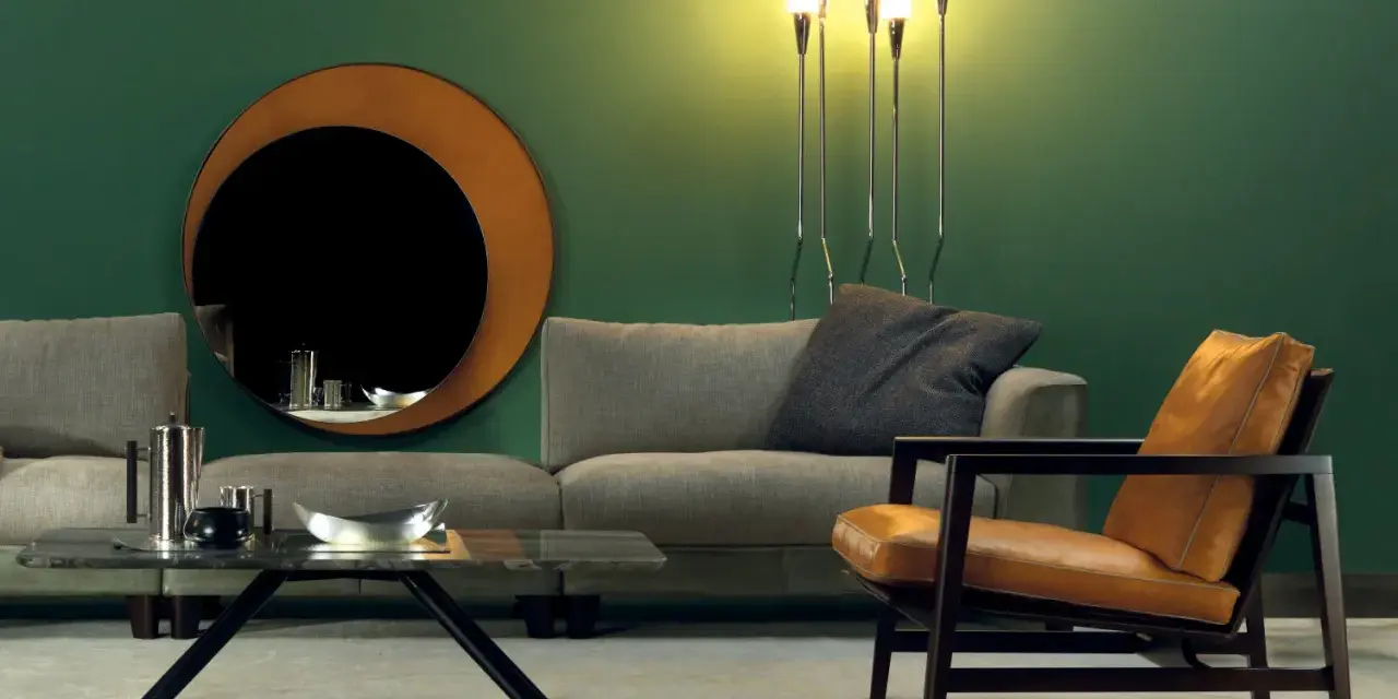 Elegante soggiorno con divano grigio, poltrona in pelle color cuoio e specchio rotondo. Idee su come abbinare divano e poltrone diverse.