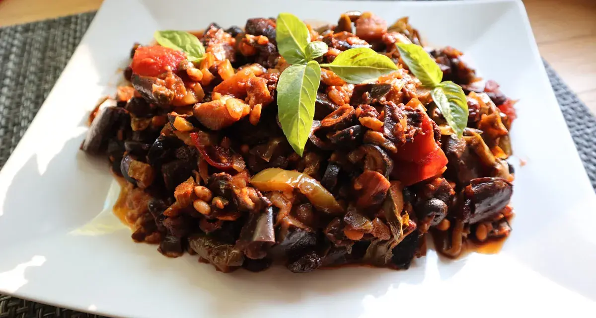 Un piatto di saporita caponata di melanzane, guarnita con foglie di basilico fresco.