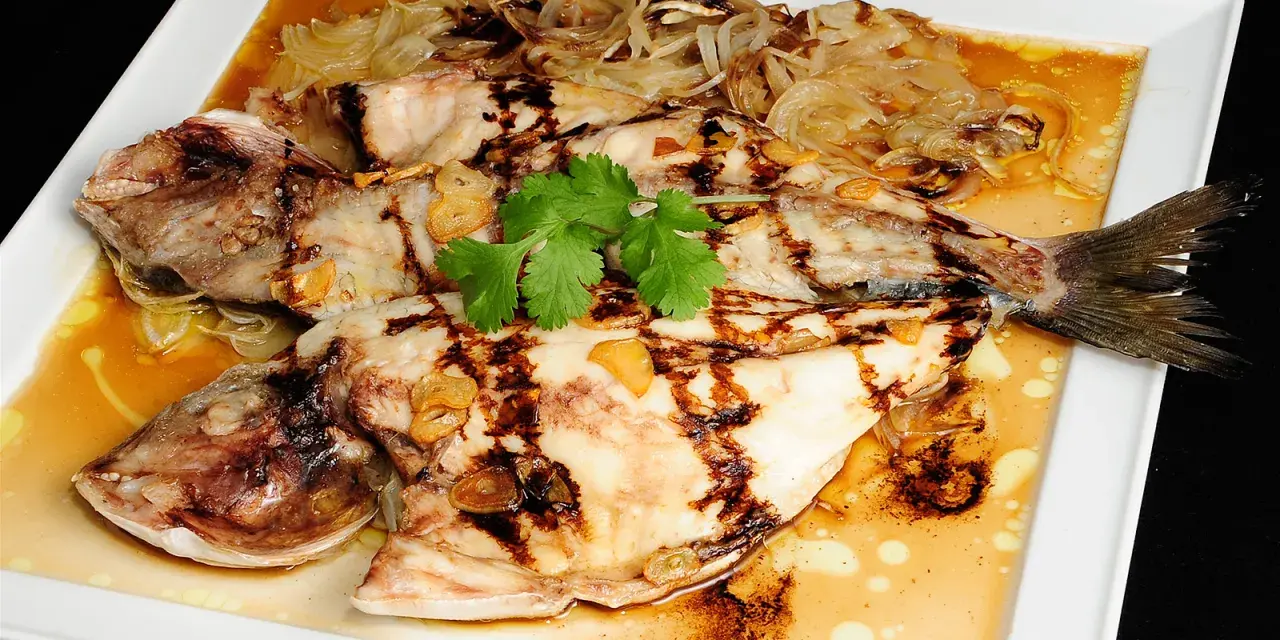 Dorada a la espalda, a la parrilla, con láminas de ajo y cebolla caramelizada, servida en salsa dorada.