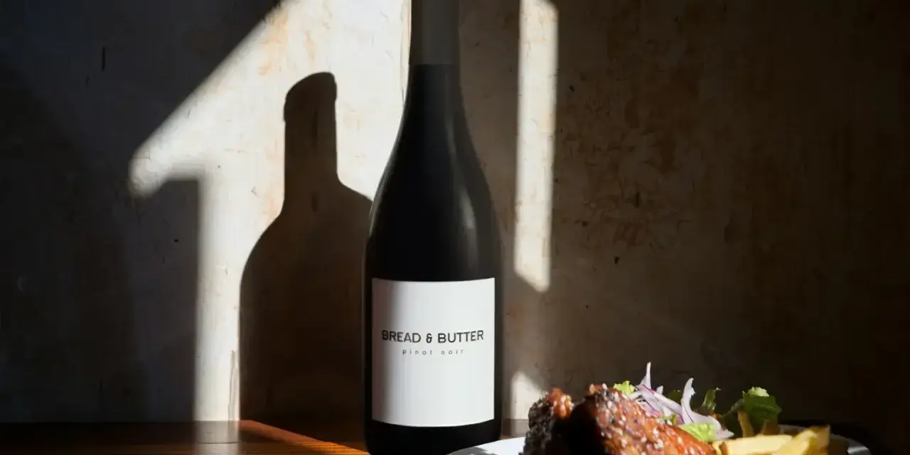 En flaska Bread & Butter Pinot Noir står bredvid en tallrik med revbensspjäll och pommes frites. Perfekt för en mysig kväll.