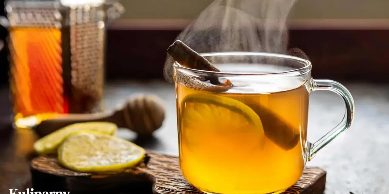 Rozgrzewająca herbata z whisky, z plastrem cytryny i laską cynamonu, paruje w szklance. Obok leżą cytryny i przyprawy.