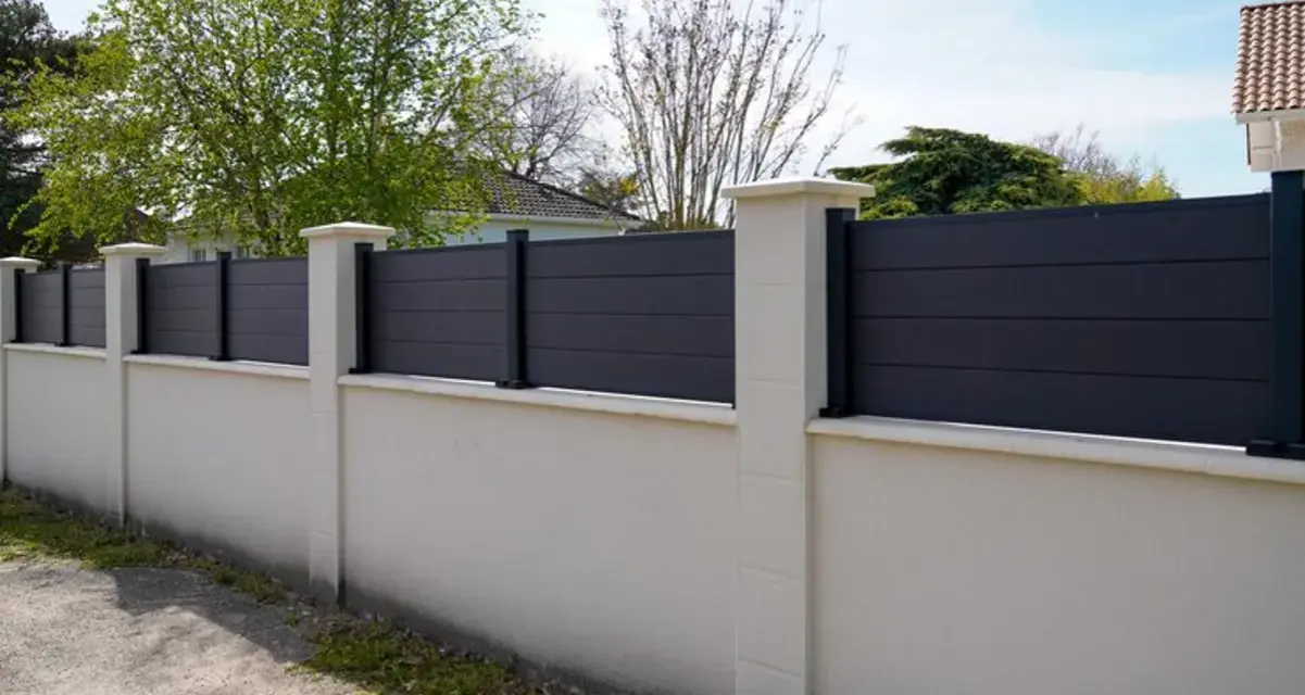 Un mur privatif moderne en composite gris, surmonté de poteaux en pierre, assure l'intimité. Distance à respecter pour une belle clôture.