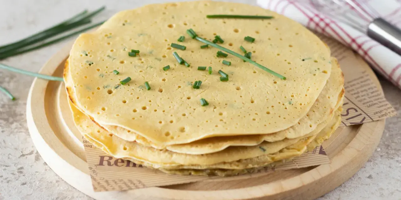 Pila di piadine di ceci dorate, guarnite con erba cipollina fresca. Perfette per un pasto leggero e gustoso.