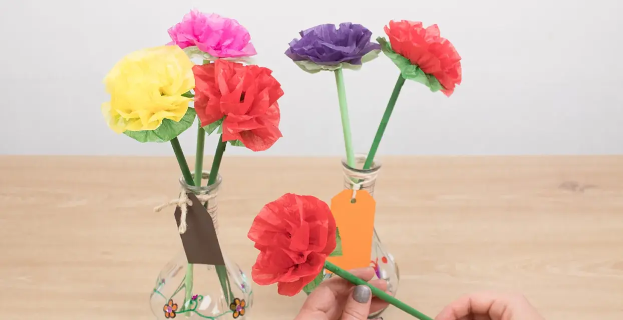 Flores de colores hechas con manualidades de papel de seda, en jarrones decorados.