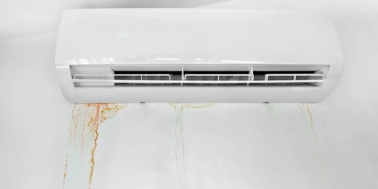 Condizionatore bianco con macchie d'acqua sul muro. La condensa gocciola, creando aloni color ruggine e verdognoli.