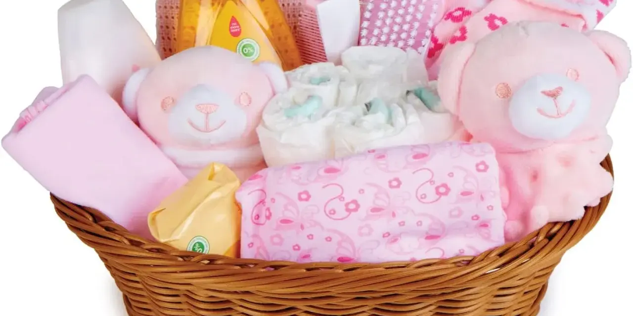 En korg fylld med rosa babyartiklar, inklusive nallar, blöjor och tvättlappar, perfekt som baby shower present.