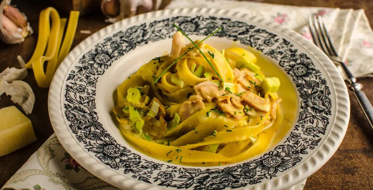 Makaron tagliatelle w kremowym sosie curry z kurczakiem i porem, ozdobiony szczypiorkiem.