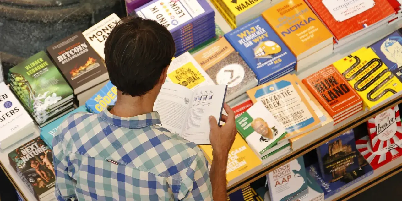 Hombre en una librería, rodeado de libros sobre finanzas y negocios, buscando las mejores editoriales para publicar un libro.