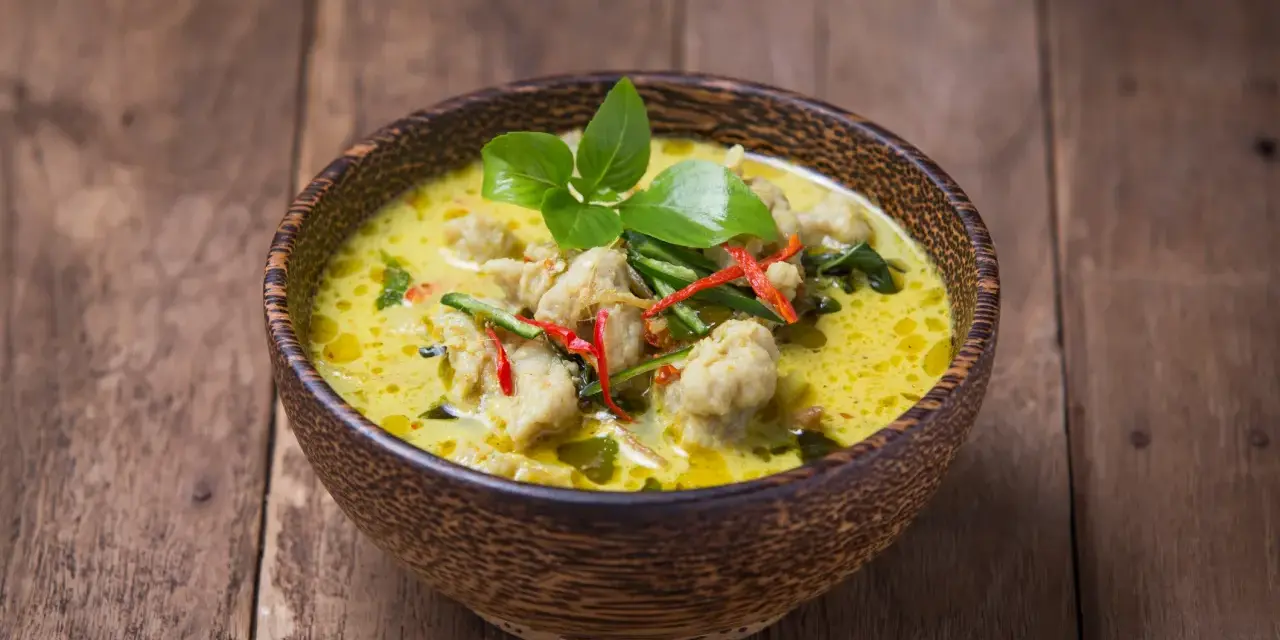 Zielone curry z kurczakiem i chili w drewnianej misce na desce.