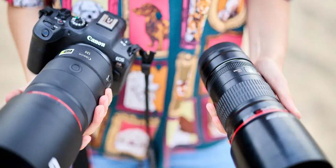 Dwie ręce trzymają obiektywy do Canona. Jeden z nich to Canon RF 135mm f/1.8L IS USM, drugi to Canon EF 135mm f/2L USM.