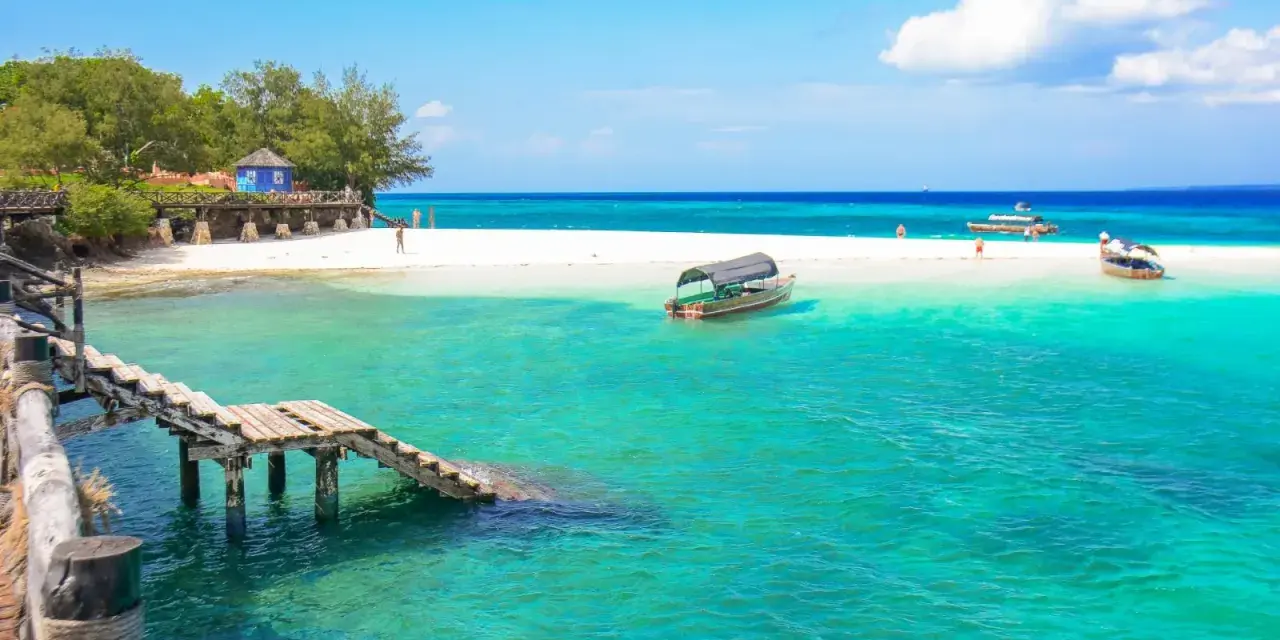 Zanzibar - wczasy opinie: turkusowa woda, biała plaża, drewniany pomost i łodzie. Rajskie widoki idealne na wakacje.
