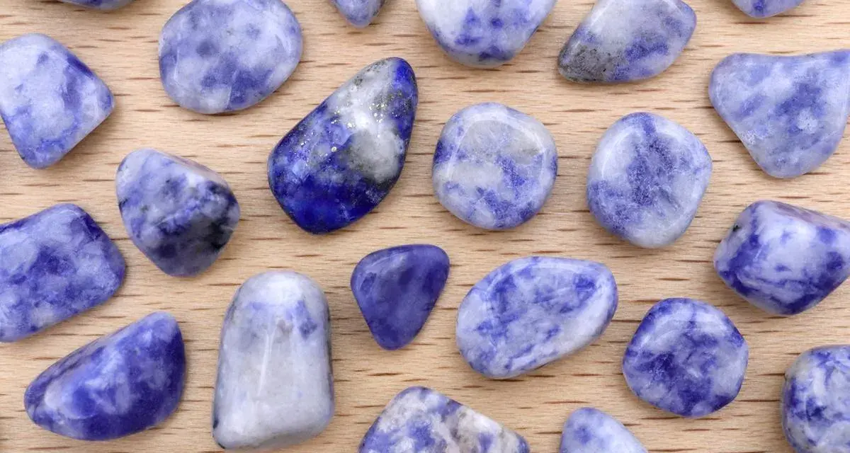 Tumbled sodalite stones, showcasing their deep blue and white patterns. Le pietre di sodalite, con le loro proprietà calmanti, sono disposte su un fondo di legno.