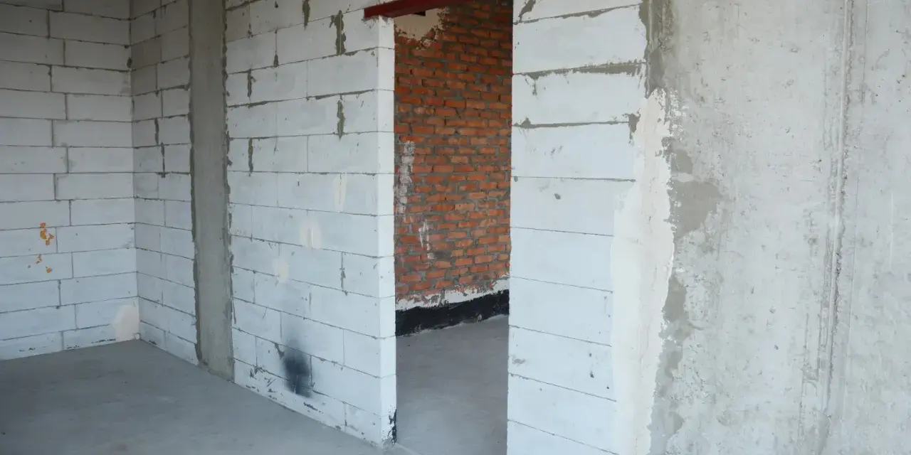 Wnętrze w budowie. Widoczny otwór drzwiowy z czerwonym nadprożem stalowym, ściany z białych pustaków i cegły.
