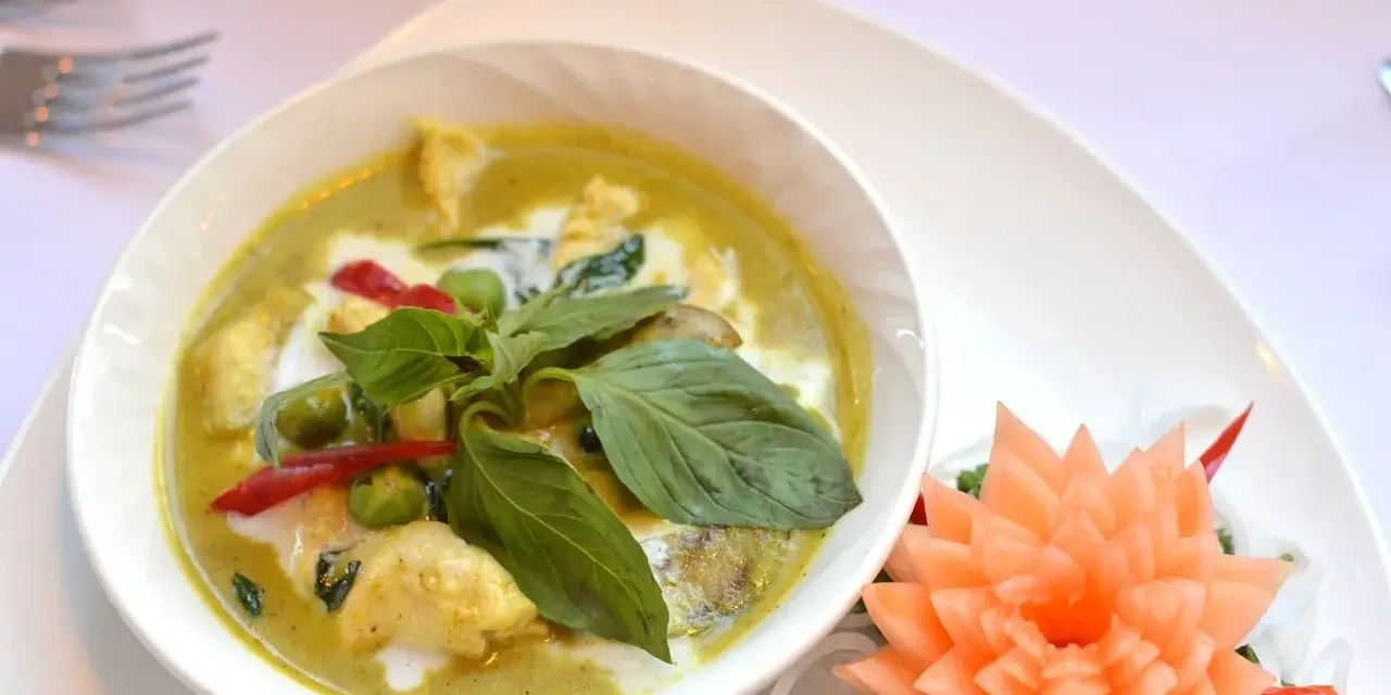 Zielone curry z kurczakiem, ozdobione bazylią i kwiatkiem z marchewki.