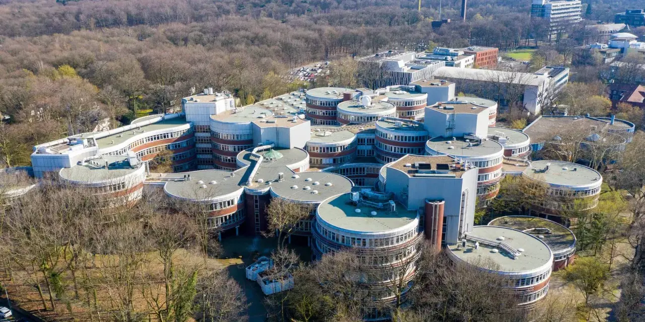 Luftaufnahme des Campus der **Uni Duisburg Essen** mit seinen charakteristischen runden Gebäuden, umgeben von Bäumen.