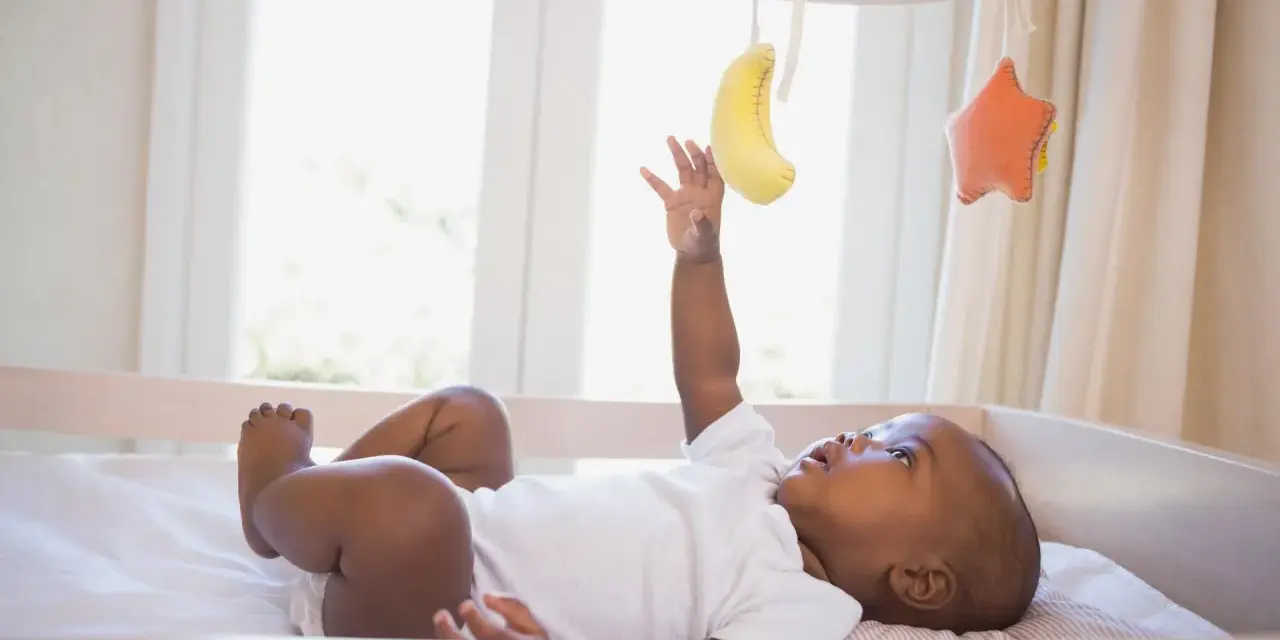 Maluch wyciąga rączkę do bananka i gwiazdki wiszących na karuzeli do łóżeczka.