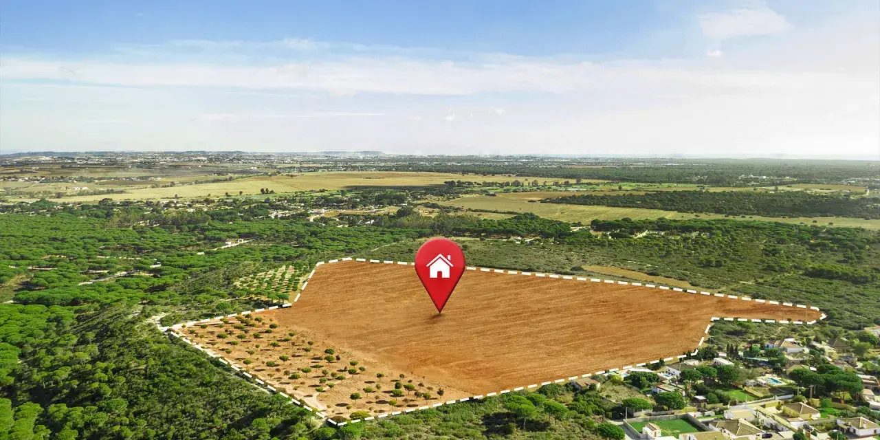 Vista aérea de varios tipos de terrenos: un campo marrón arado, un bosque de pinos y un área residencial.