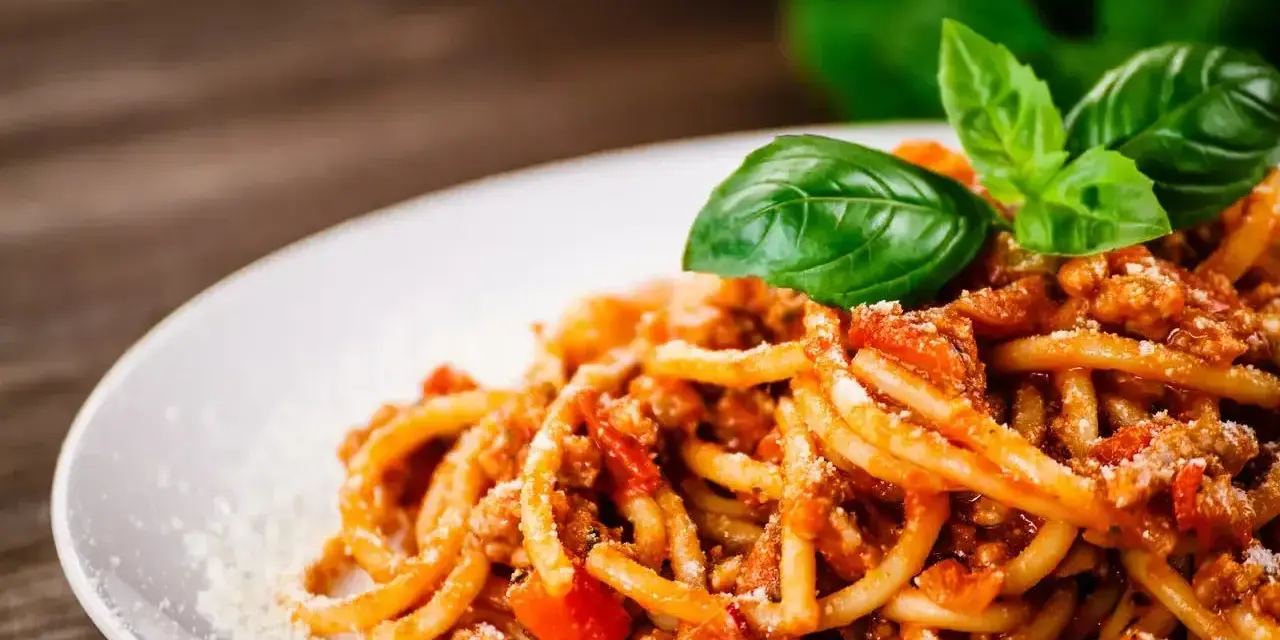 Prosty przepis na spaghetti z mięsem mielonym, podane na białym talerzu, ozdobione listkami bazylii i posypane parmezanem.