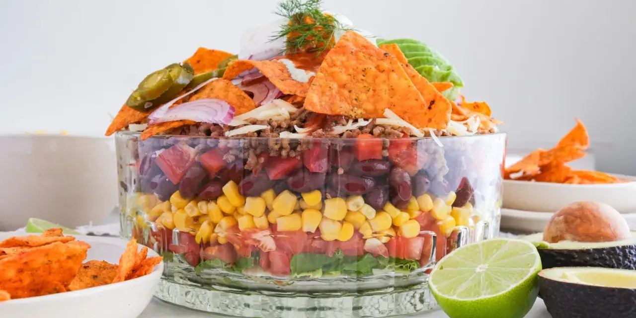 Schichtsalat mit Tortilla-Chips, Bohnen, Mais, Tomaten und Hackfleisch. Ein köstlicher, vegetarischer Nacho Salat, garniert mit Jalapeños und Sauerrahm.