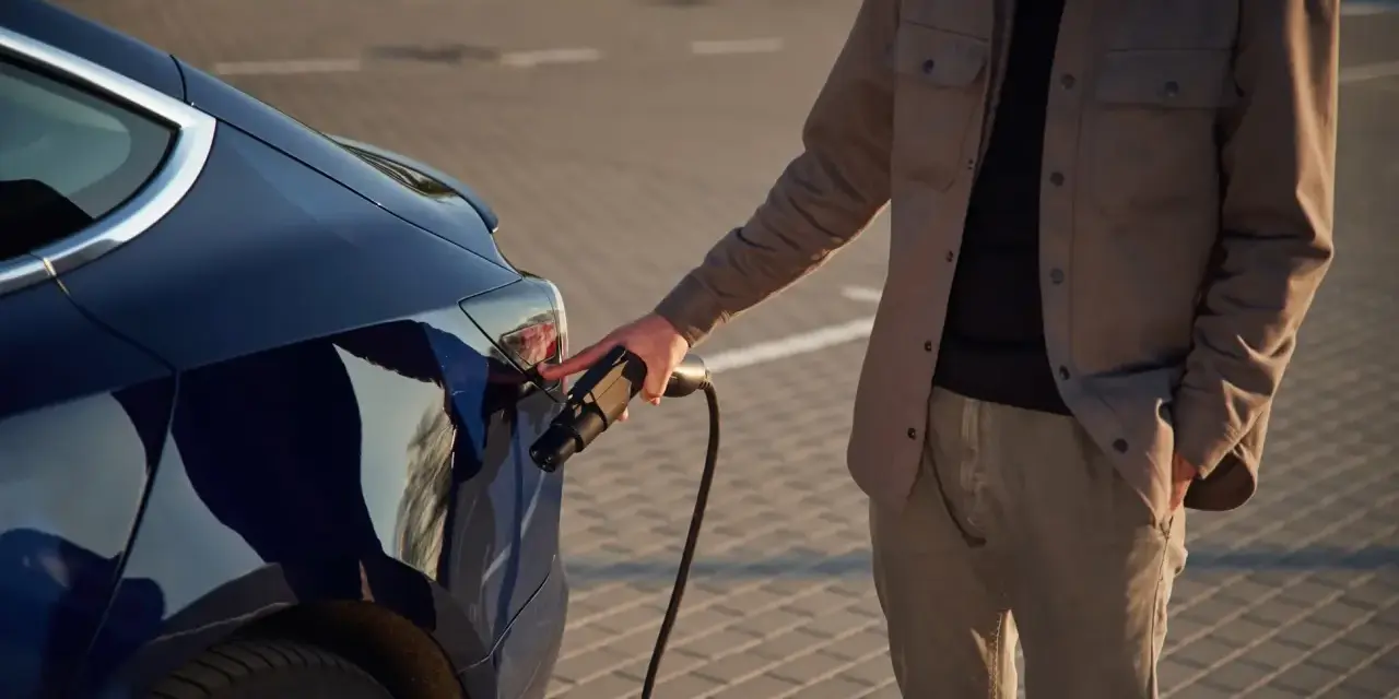 Mężczyzna podłącza ładowarkę do ciemnoniebieskiego samochodu elektrycznego. Zastanawiasz się, ile kosztuje ładowanie samochodu elektrycznego?