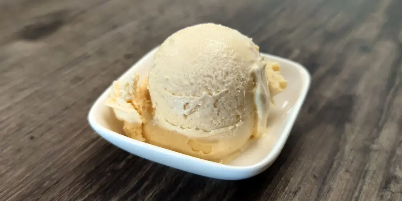 Cremiges Dulce de Leche Eis in einer weißen Schale auf Holzhintergrund.