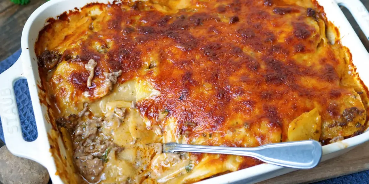 Omas Kartoffelauflauf mit Hackfleisch, goldbraun überbacken, dampft in einer weißen Auflaufform. Eine Gabel steckt in der saftigen Schicht.