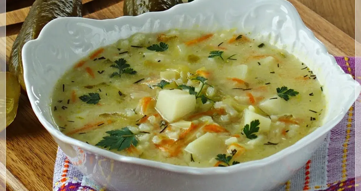 Aksamitna zupa ogórkowa na żeberkach, pełna ziemniaków, marchewki i koperku, z ogórkami w tle.