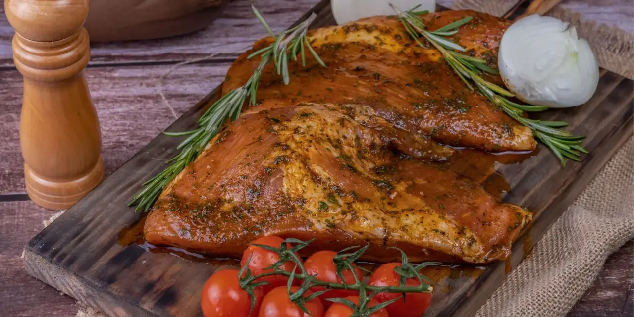 Carne marinada, lista para cocinar. El secreto ibérico se revela con romero, tomates y cebolla.