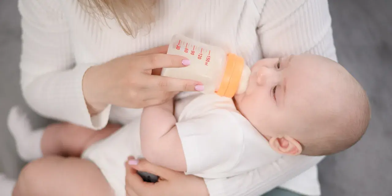 Mama karmi dziecko mlekiem modyfikowanym z butelki. Dziecko pije spokojnie, a mama czule go trzyma.
