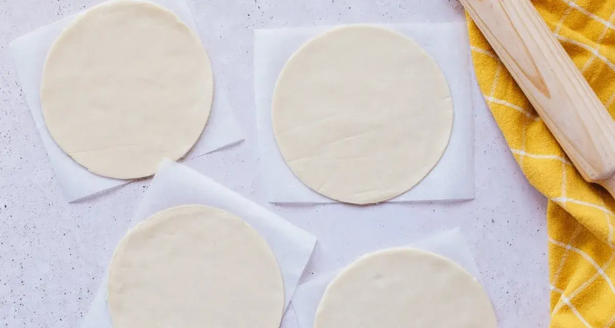 Cuatro discos de masa empanada listos para rellenar, junto a un rodillo y un paño amarillo.