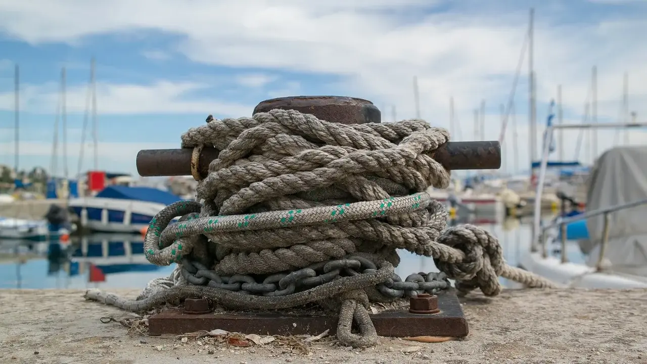 Grosse amarre enroulée sur une bitte d'amarrage, prête à supporter le poids d'un bateau. Le diamètre de la corde suggère une grande résistance.