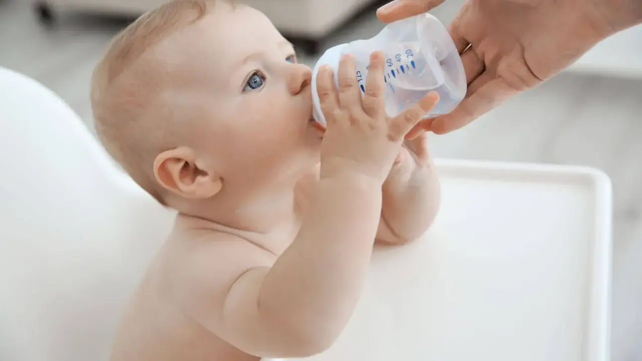 Niemowlę pije wodę z butelki. Od kiedy dziecko może pić wodę mineralną nieprzegotowaną? Od 6. miesiąca życia, gdy zaczyna rozszerzać dietę.