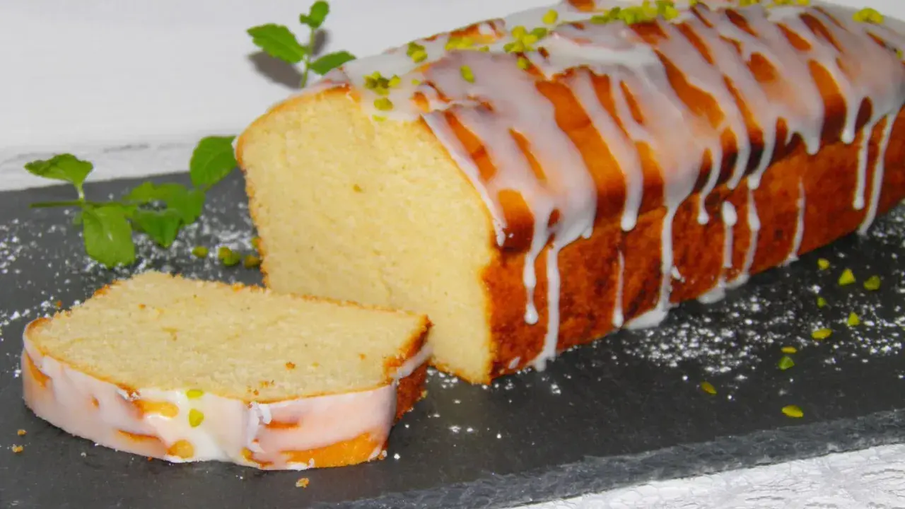 Ein saftiger mallorquinischer Zitronenkuchen mit Zuckerguss und Pistazien, daneben ein angeschnittenes Stück.