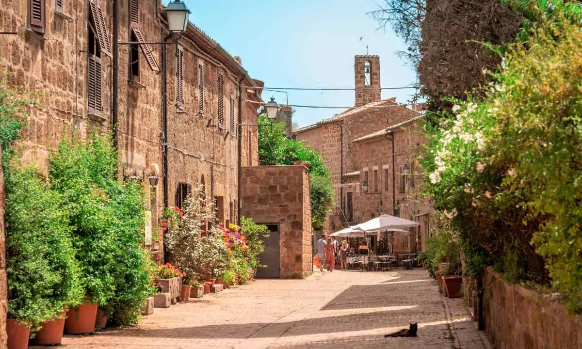 Un borgo medievale con case in pietra, fiori colorati e un gatto nero che riposa al sole. Un'idea per scoprire i paesi vicino a Grosseto da visitare.