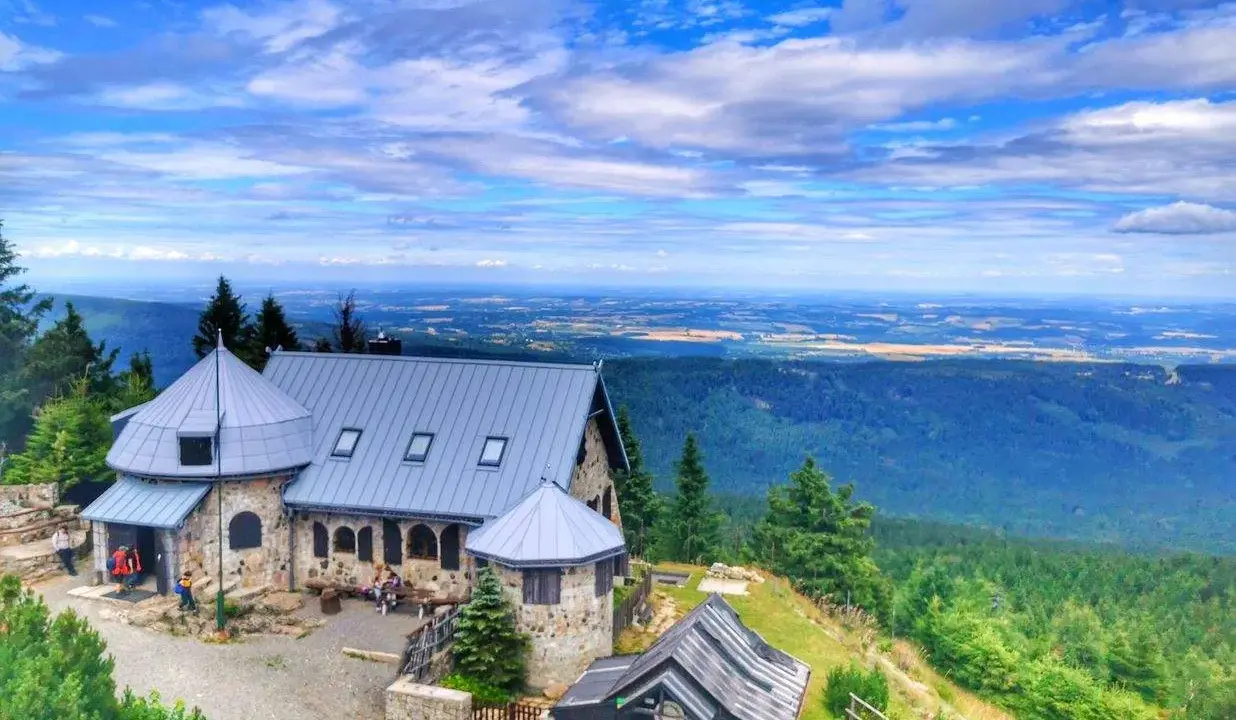 Kamienny budynek na szczycie góry, z którego roztacza się widok na rozległą dolinę. Wysoki kamień stanowi część architektury.