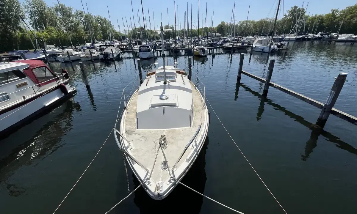 Un voilier blanc, type Westerly Centaur, est amarré dans un port. D'autres bateaux sont visibles au loin.