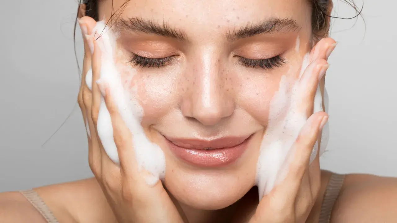 Donna con gli occhi chiusi mentre si lava il viso con un detergente schiumoso. Un gesto delicato per capire come si usa il detergente viso.