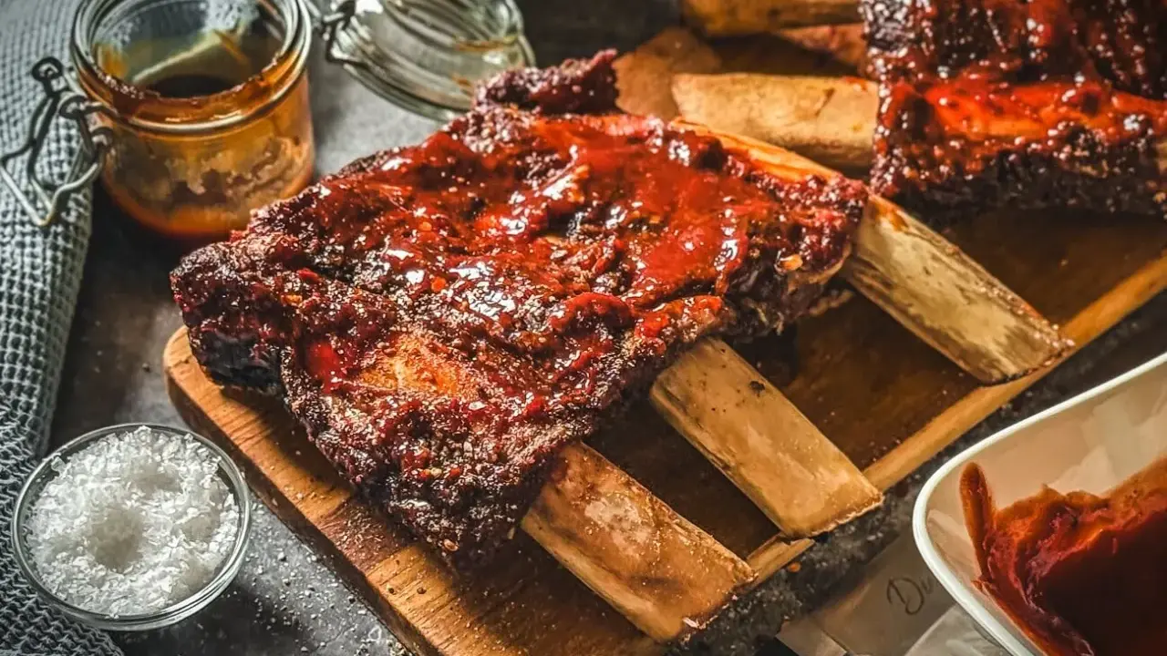 Saftige Rippchen mit BBQ-Sauce, perfekt für Ihre nächsten Grill Rezepte. Dazu grobes Salz und eine Schüssel Sauce.