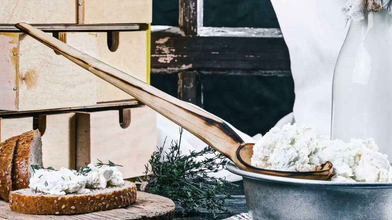 Fromage blanc frais, parfait pour une recette fromage blanc yaourtière. Servi sur du pain avec des herbes, à côté d'une bouteille de lait.