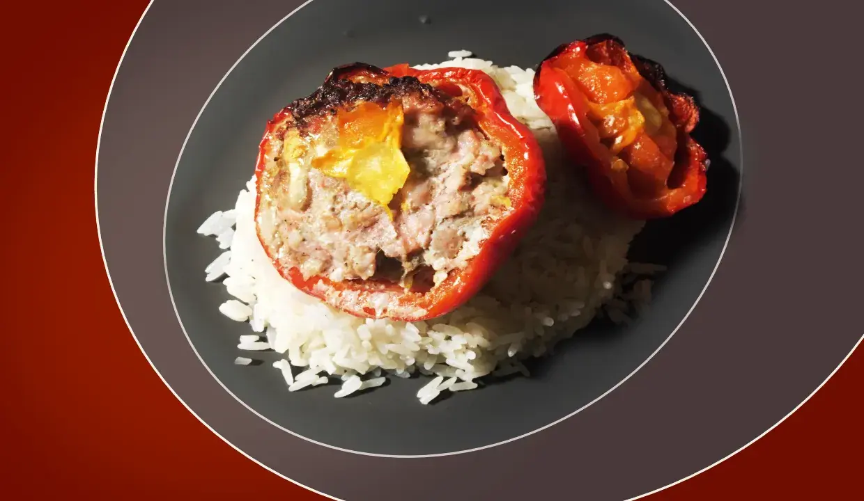 Poivrons rouges farcis à la viande, servis sur un lit de riz blanc. Une sauce légère accompagne ce plat, rappelant les saveurs des tomates farcies.