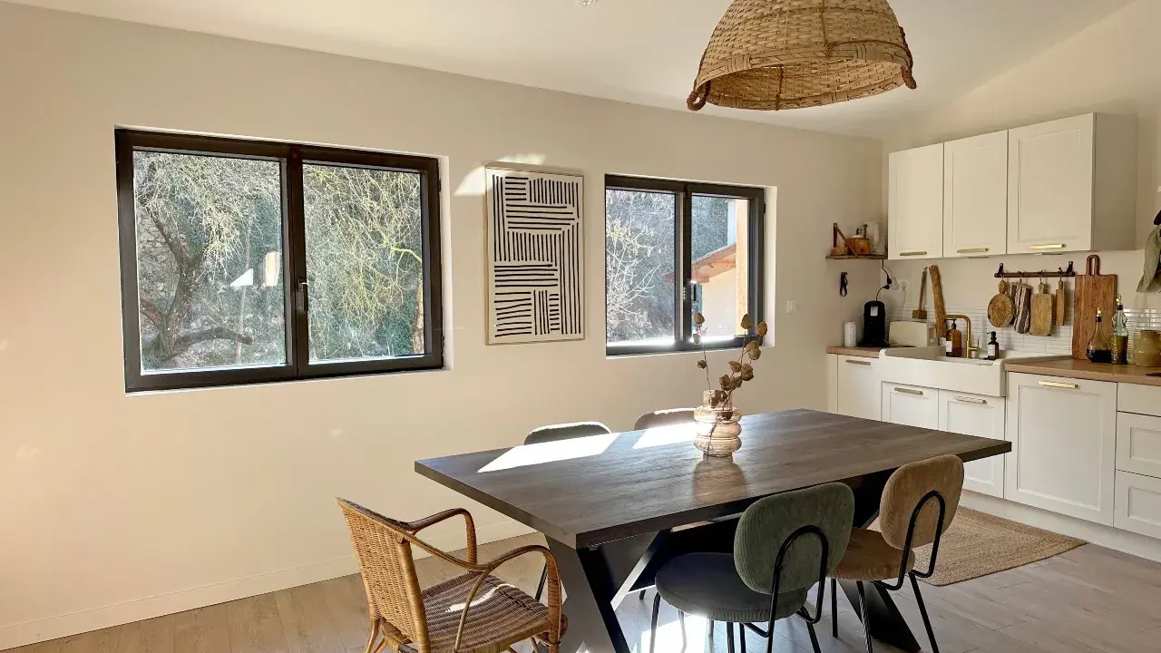 Comedor y cocina luminosos con mesa de madera, sillas de mimbre y tapizadas, y ventanas de cristal térmico que dejan ver el exterior.