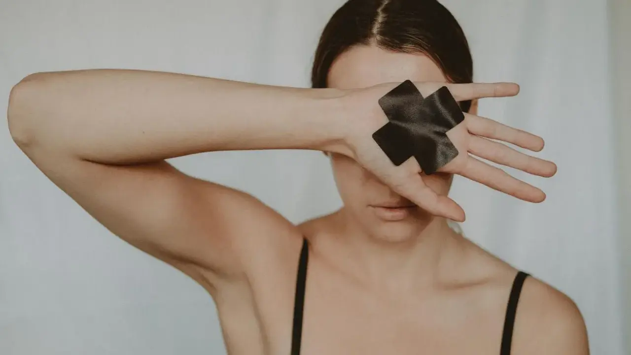 Dłoń z czarną taśmą w kształcie krzyża zakrywa oko, symbolizując traumę seksualną i potrzebę ochrony.
