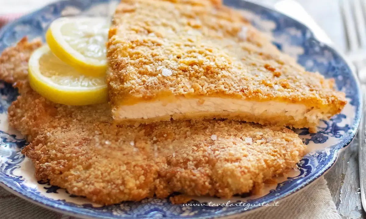 Due cotolette al forno dorate e croccanti, servite su un piatto blu e bianco con spicchi di limone.