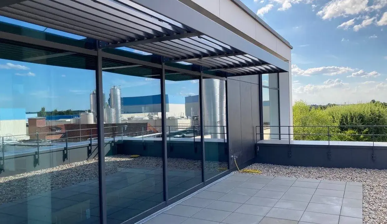 Moderne Dachterrasse mit Glasfront und Lamellendach. Ein gelber Schlauch liegt bereit, um das Flachdach anzuheben und zu pflegen.