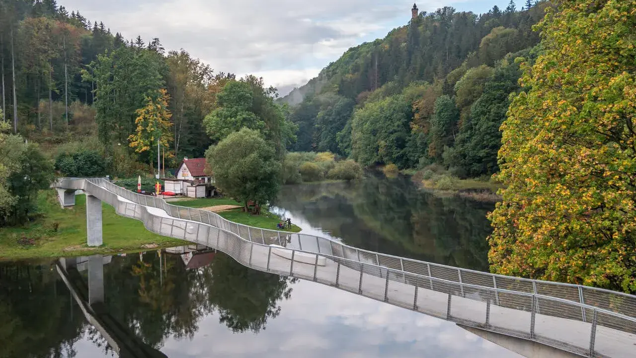 Idealna wycieczka na niedzielę na Dolny Śląsk: nowoczesny most nad spokojną rzeką, otoczony jesiennym lasem i wieżą widokową na wzgórzu.