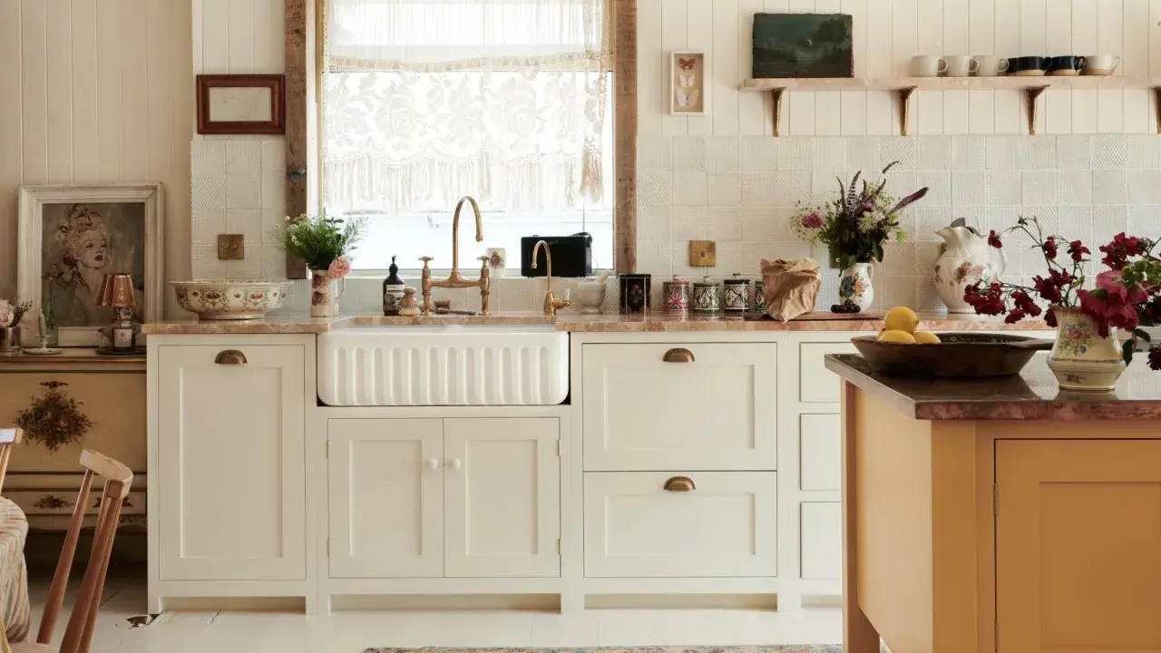 Urocza kuchnia retro inspiracje: białe szafki, ceramiczny zlew, mosiężna armatura, koronkowy zazdrostka i stylowy dywanik.