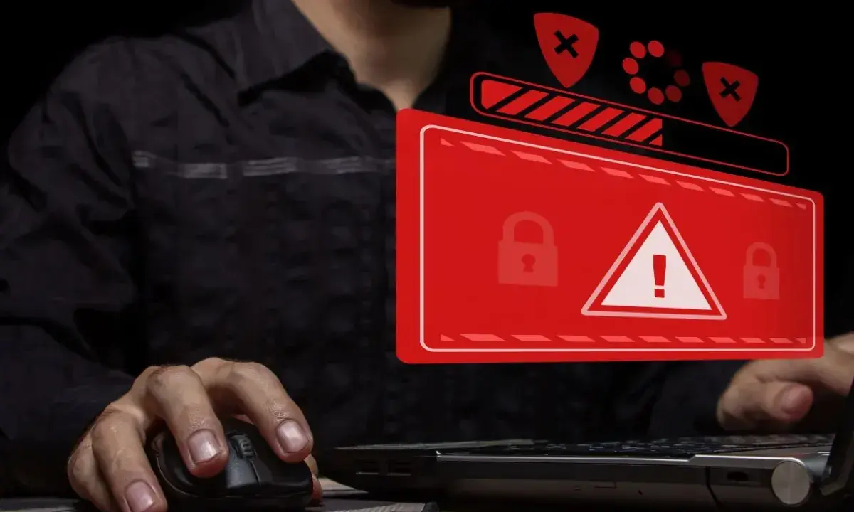 Osoba przy komputerze, na ekranie ostrzeżenie o zagrożeniu i blokadzie. To obrazuje problem cyberprzestępczości.